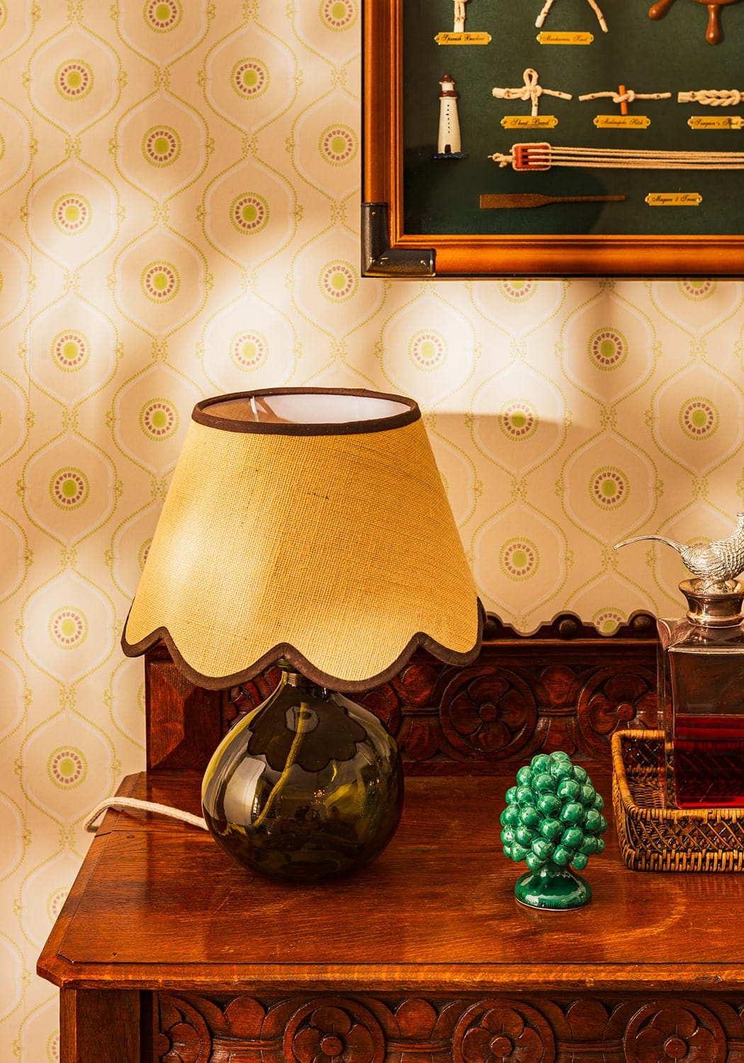 A vintage table lamp with a dark green glass base and a brown jute scallop fabric lampshade in beige