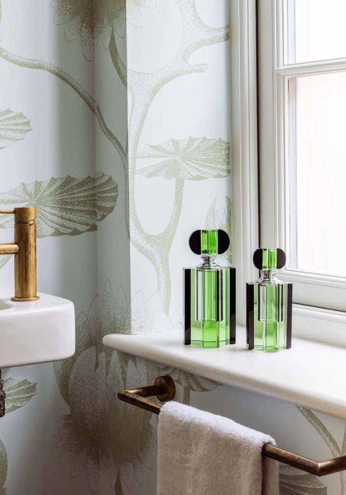 Two emerald green glass chrysler building scent bottles with black caps sit on a white windowsill
