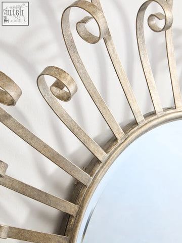 A cissell spoke style wall mirror featuring a sunburst design with a distressed silver ornate metal frame and scrollwork