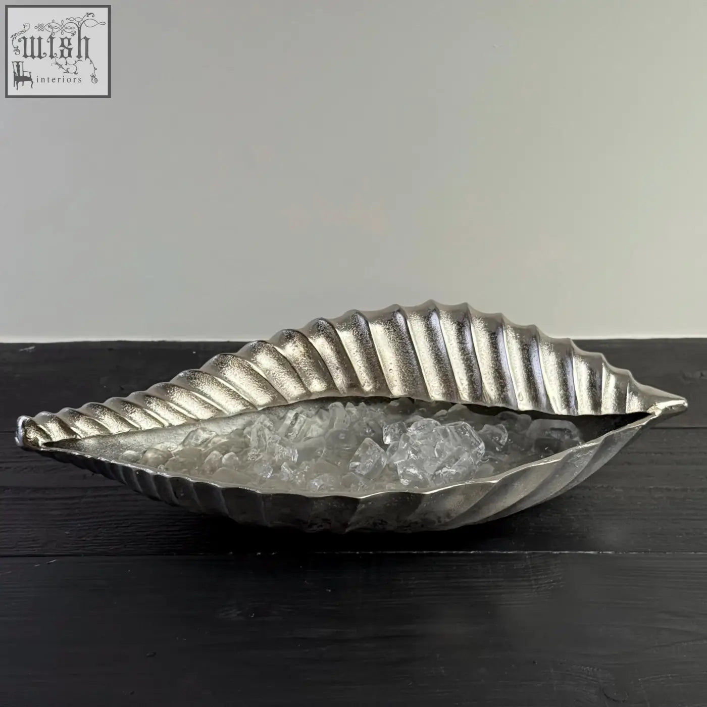 Silver metallic clam shell champagne ice bucket with ridged texture and slightly open cast design for chilling wine