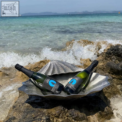 Two dark green glass bottles of château sire sparkling wine sit inside a silver clamshell solid champagne ice bucket
