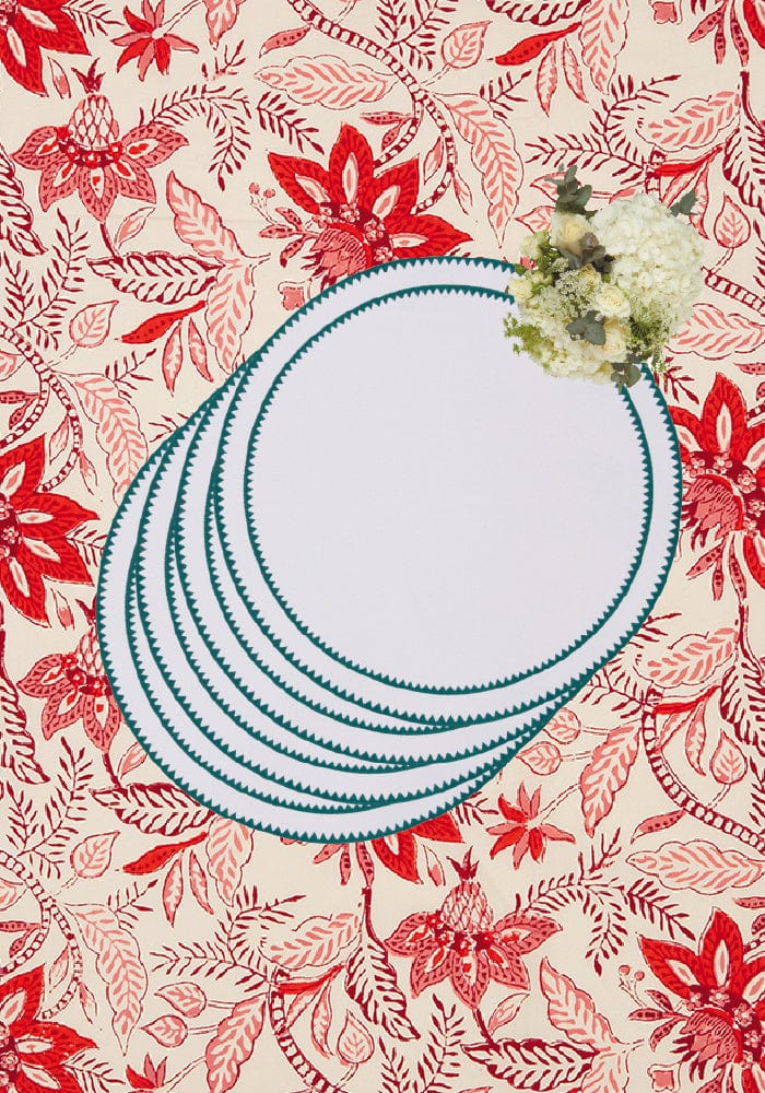 Stack of white ceramic plates with teal scalloped edges on a red floral tablecloth with classic green round placemats