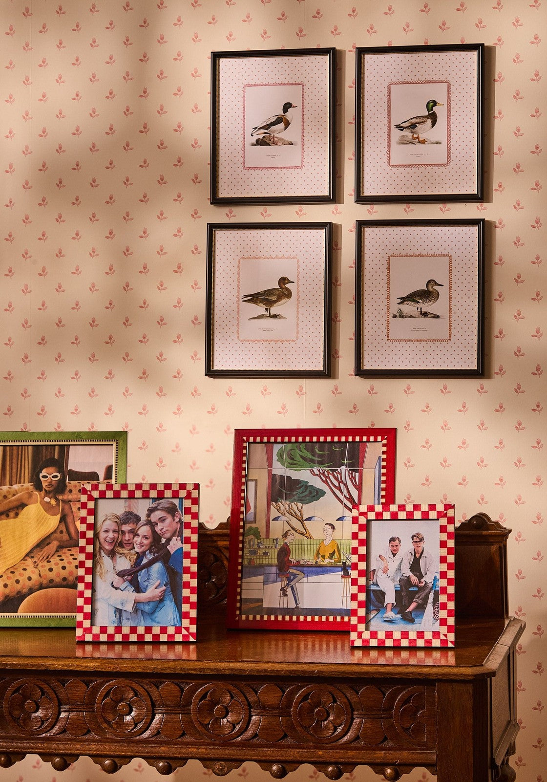 Four framed duck illustrations with black frames on pink dotted backgrounds above a wooden console with a classic red checkered frame 7x5