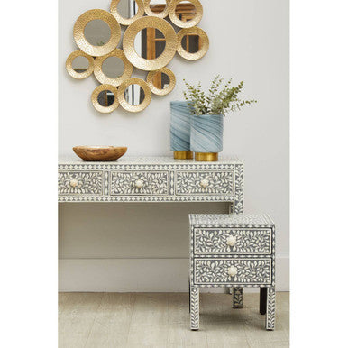 Silver and white bone-inlaid console table with intricate floral carvings beside a large grey glass vase