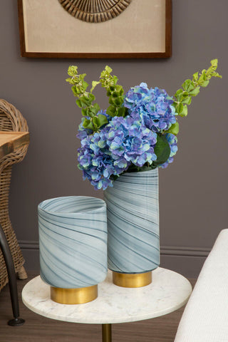 Two large grey glass vases with gold bases and a swirling pattern holding vibrant purple hydrangeas