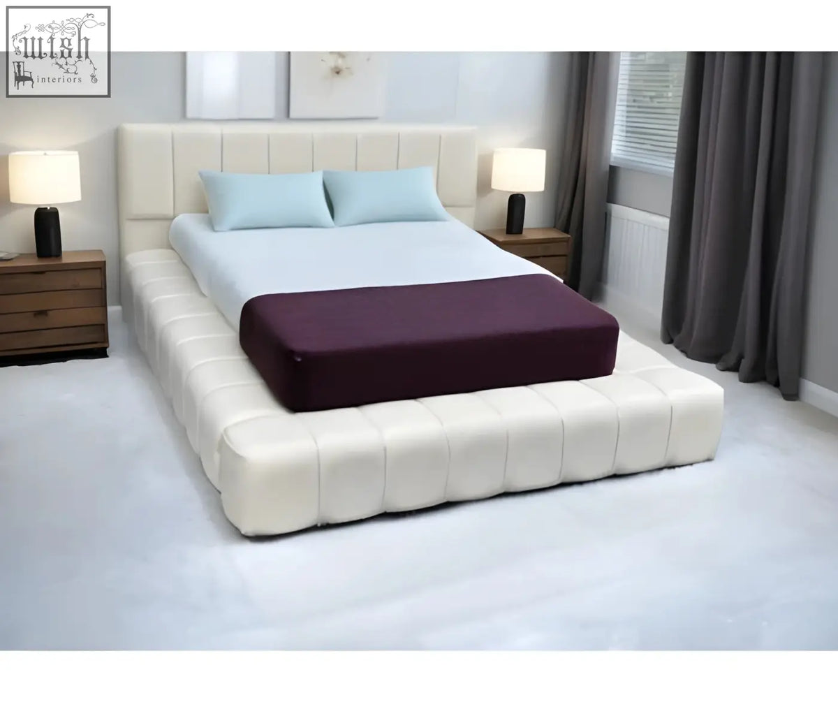 Cream-colored tufted cloud bed frame with matching headboard and dark purple mattress cover foot end view