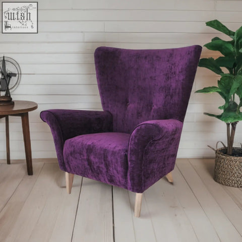 A plush deep purple velvet coco wing chair with tufted back and rolled arms on light wooden legs