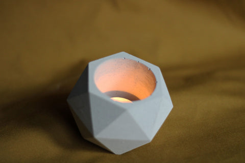 A light gray concrete hexagonal pot candle holder with a faceted design glowing with an orange candle inside