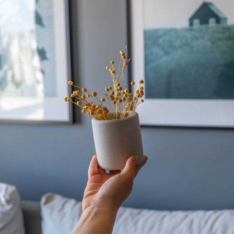 Minimalist white ceramic vase with dried golden-yellow flowers next to a concrete pen-pencil holder for desk use
