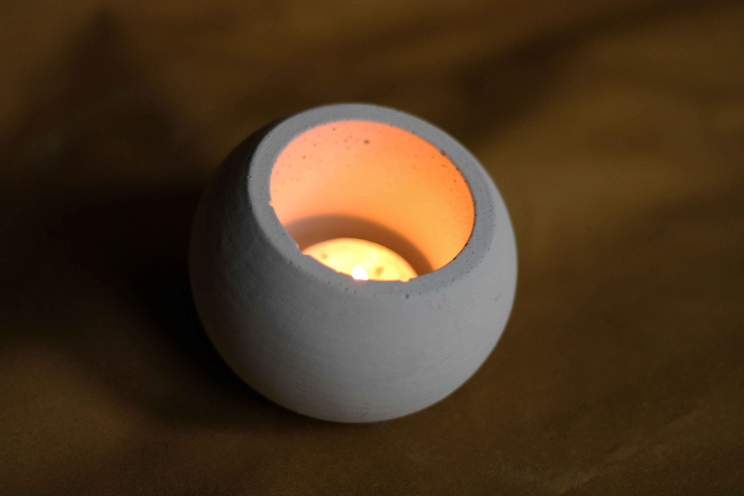 A minimalist white concrete round pot candle holder with a smooth matte finish holding a small lit candle