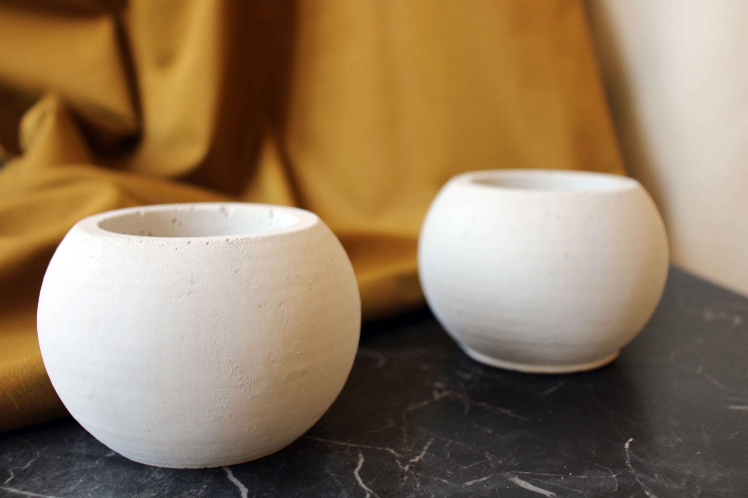 Two minimalist white ceramic round pots with matte finish and subtle texture on dark marble surface concrete round pot