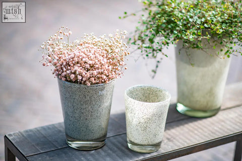 A speckled gray conic vase from dutz collection made of mouth blown thick glass with bubbles holding pink and white babys breath