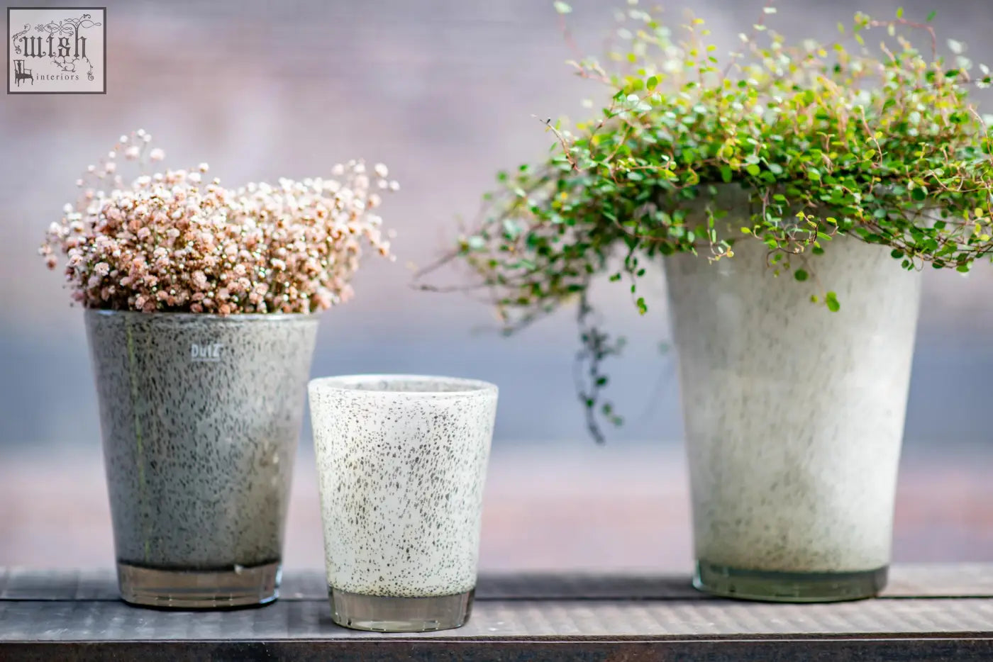 Three speckled ceramic planters with greenery and flowers featuring dutz collection mouth blown glass design