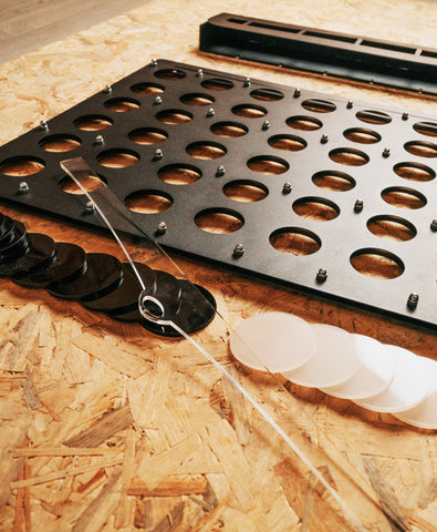 Black metal connect 4 board with circular cutouts silver screws and black and white translucent stopper piece discs