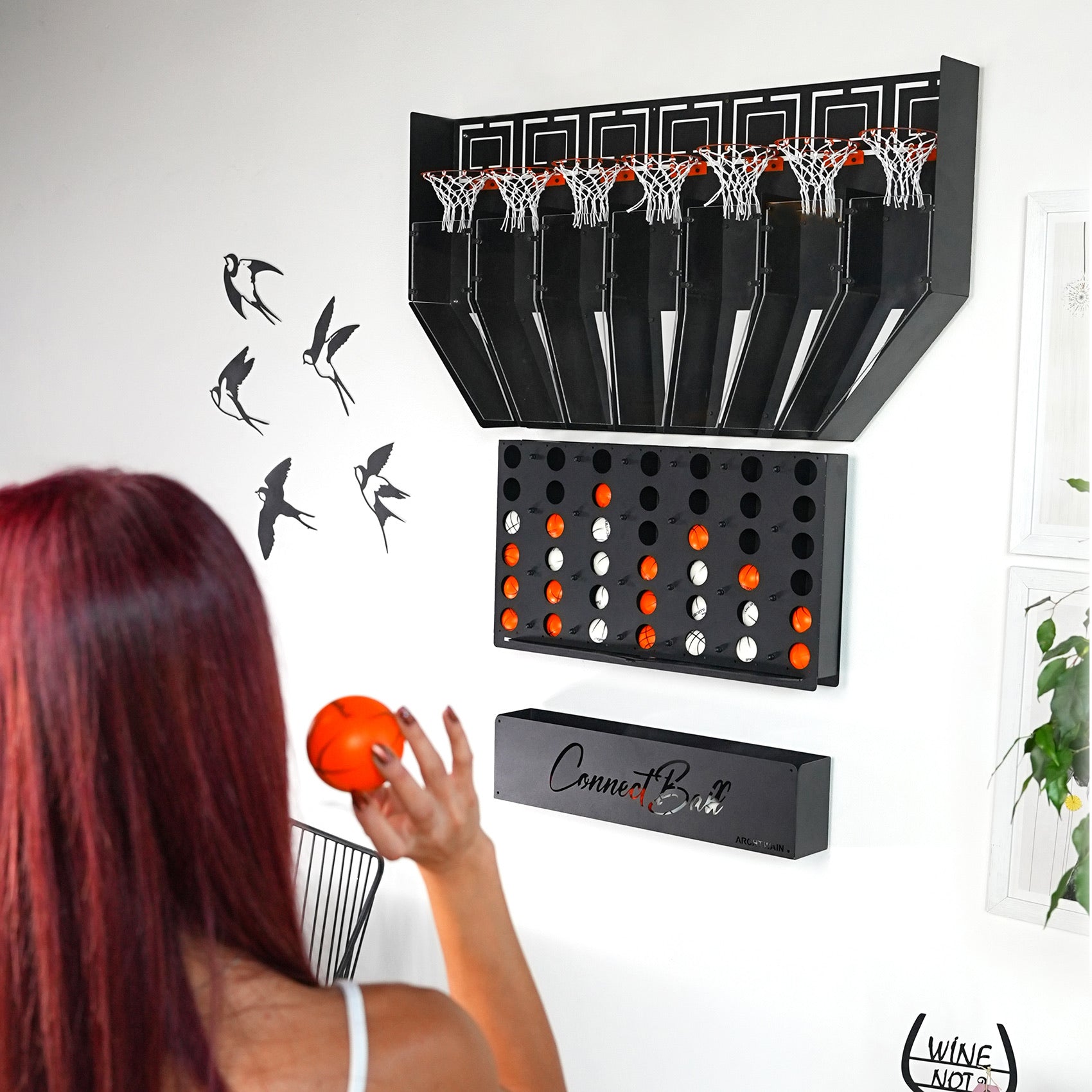 Black wall-mounted connect balls game with four balls and a central piece grid of orange and white balls below