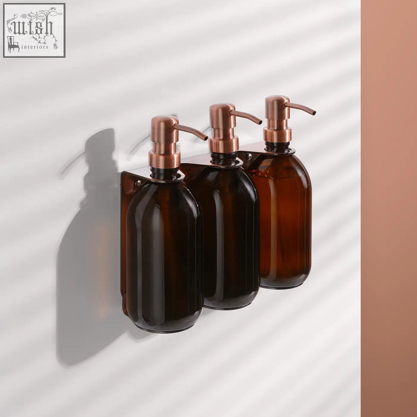 Copper triple wall-mounted soap dispenser with three amber glass bottles and rose gold pump heads on a bracket