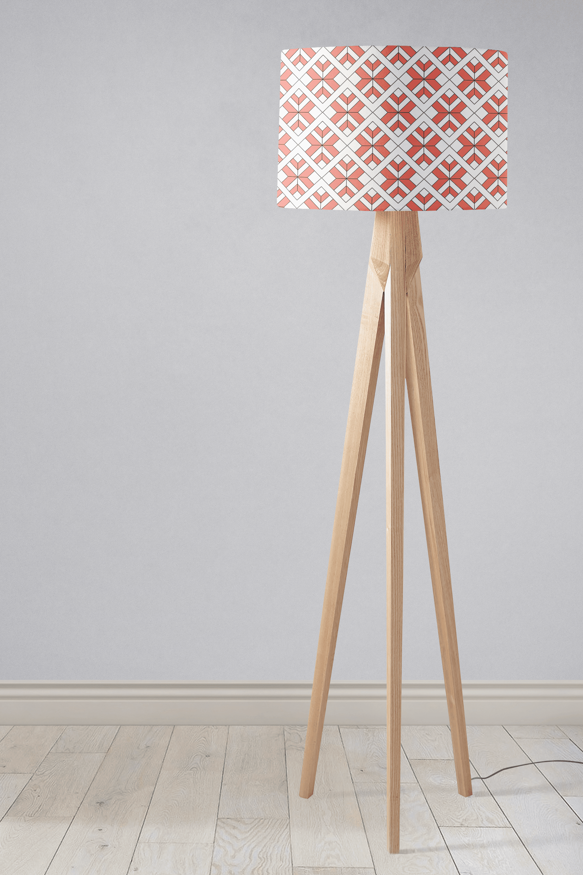 A modern tripod floor lamp with a coral and white geometric design lampshade and slender wooden legs perfect as a table lamp