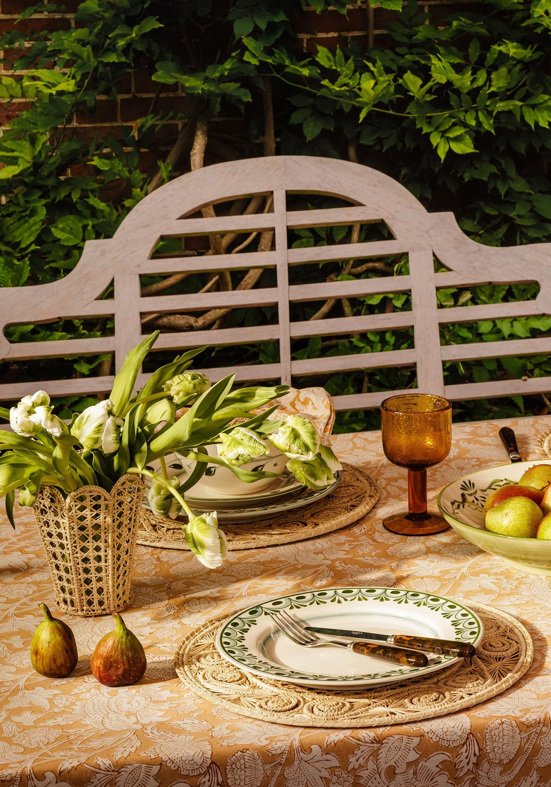 A delicate white ceramic cordelia dinner plate with a green floral border on an ornate woven placemat