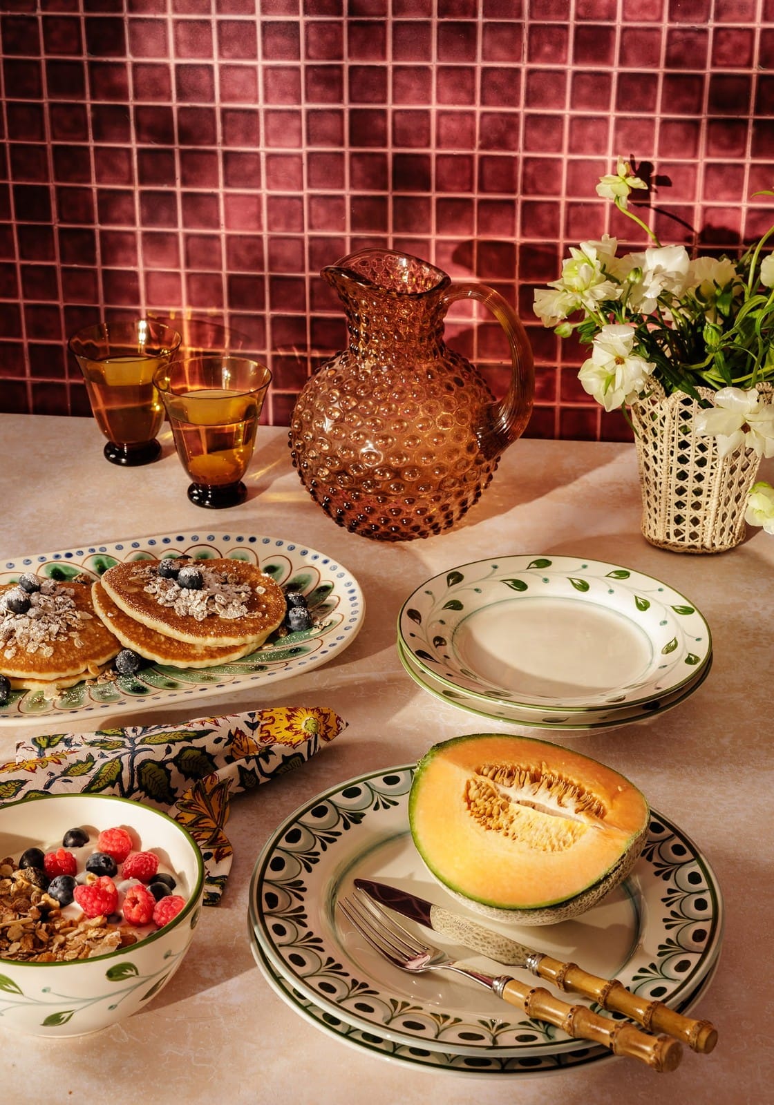 A brown textured glass pitcher with handle and spout on table next to a green cordelia side plate
