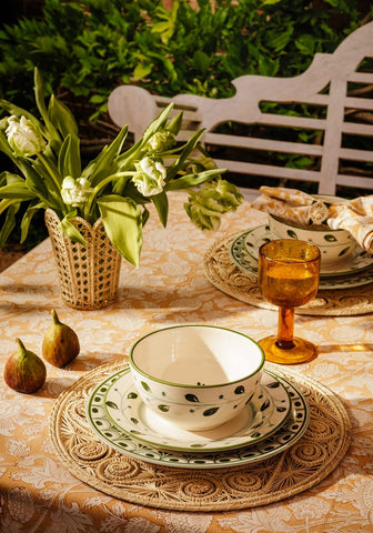 White ceramic cordelia side plate with green leaf patterns and matching rim set on a decorative plate