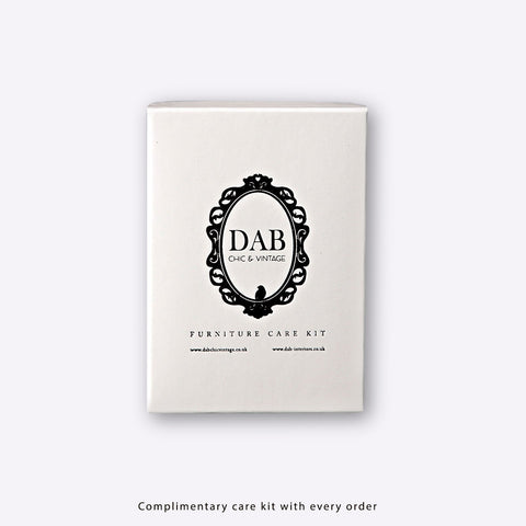 White rectangular box with black ornate logo for dab chic vintage furniture care kit next to corner tv units with black steel legs