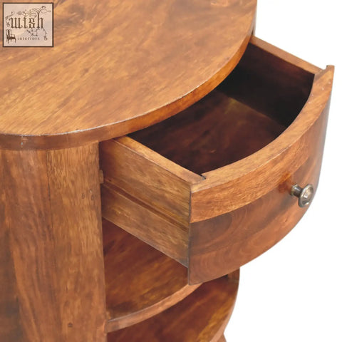 A warm medium-brown solid mango wood cortez chestnut bedside table with a round top and curved drawer with silver knob