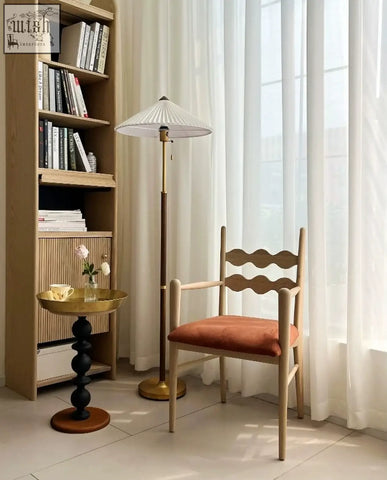 A wooden chair with a wavy backrest and orange seat next to a cosmo round side table with gold tray for a delightful blend