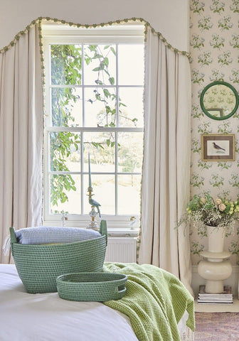 Green woven rattan cotswolds oval storage baskets with handles sitting on a bed set of 2