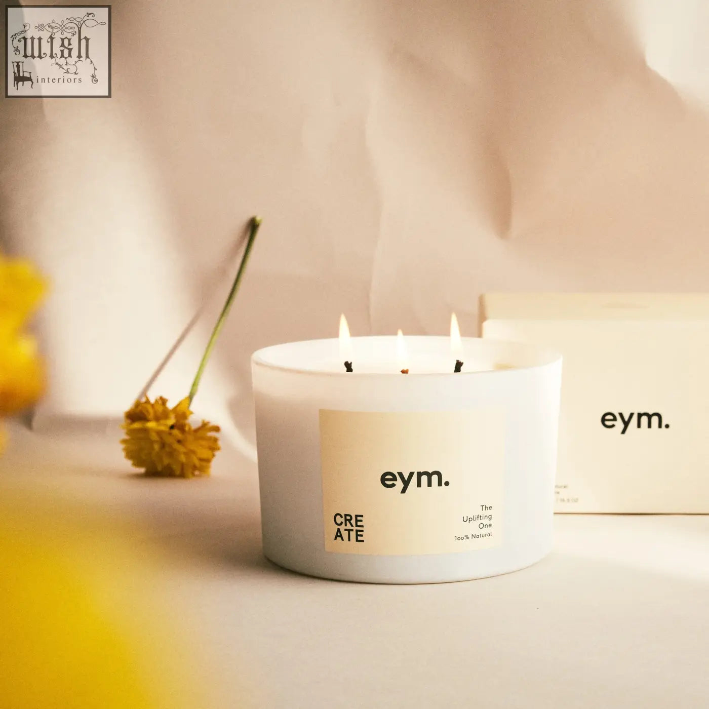 Create three wick white candle with beige eym label in glass container featuring three lit wicks