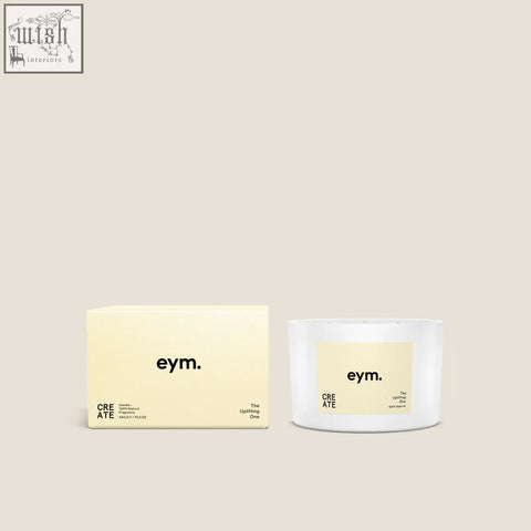 White cylindrical three wick candle with pale yellow label reading eym the uplifting one in minimalist black font