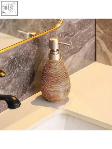 A retro style teardrop soap dispenser with a woven golden brown ceramic body and metallic pump for hand soap use