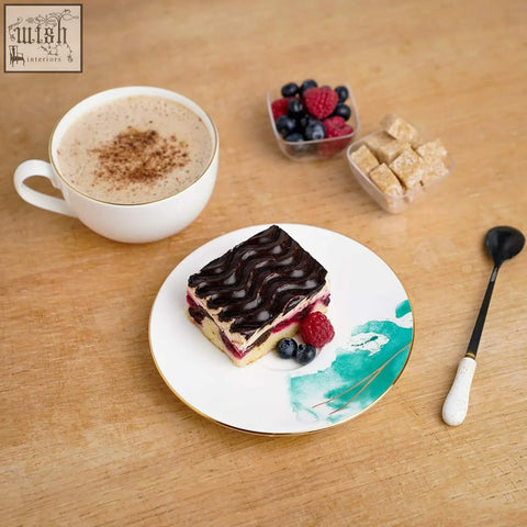 A slice of chocolate-swirled berry cake on a white premium porcelain cup and saucer with teal design and gold banding
