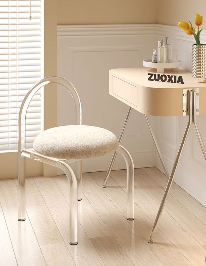 A sleek curved clear plastic dressing table chair with a plush off-white cashmere seat pad