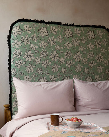 A sage green curved frill headboard with white floral pattern and black fringed trim made from natural linen by micaela sharp