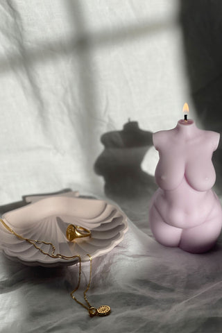 A lit pale pink curvy body candle shaped like a human torso with a flame on top and 1px solid edges