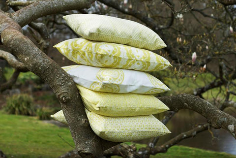 Stack of light green and white celery trellis cushion covers with patterned throw pillows resting on tree branches