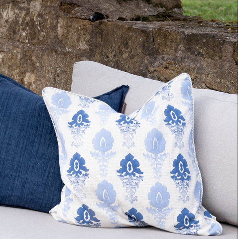 A white cushion cover with blue fleur ombre floral pattern and embroidered border in light blue accents