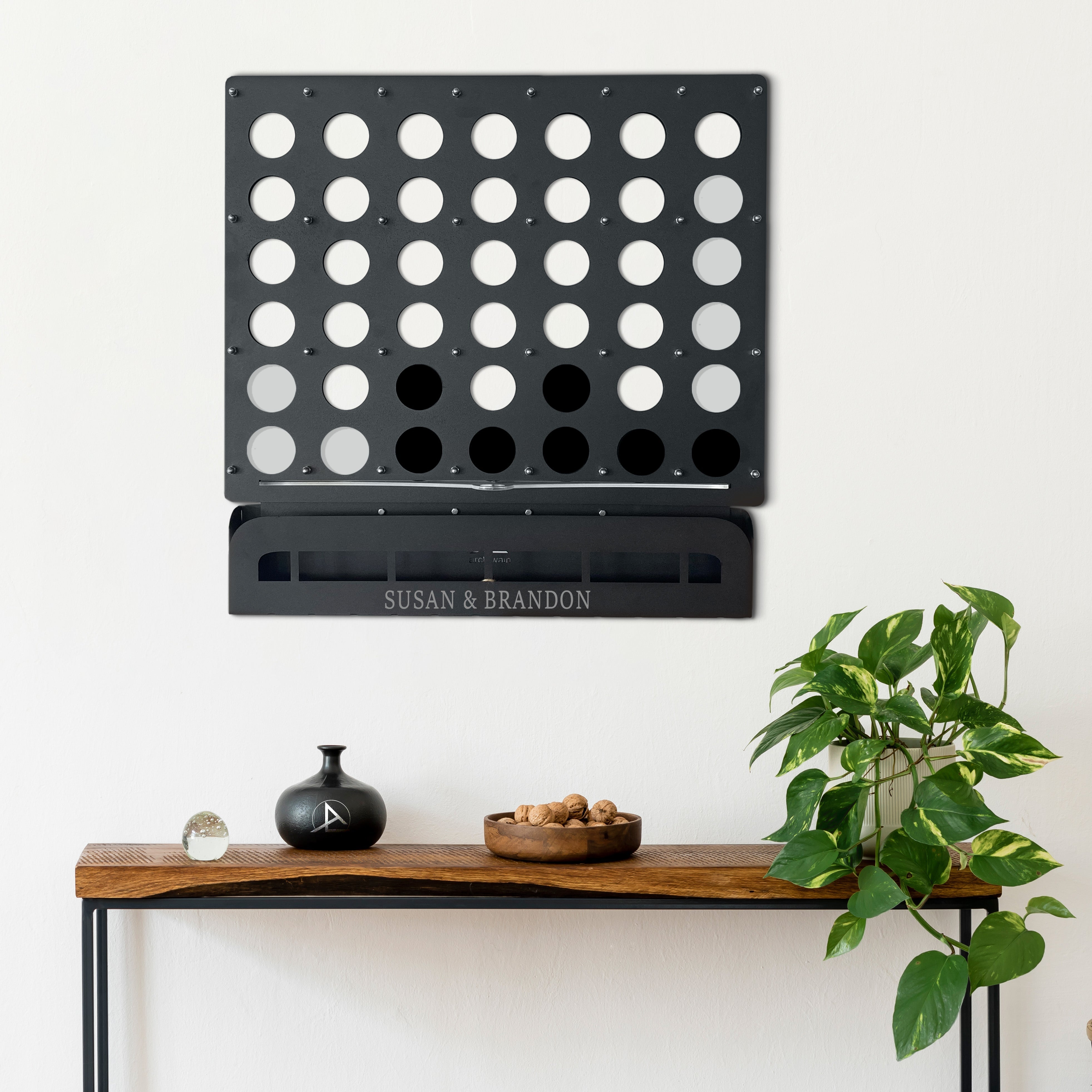 Customized black metal connect four wall game with engraved names susan and brandon on the base for fun play