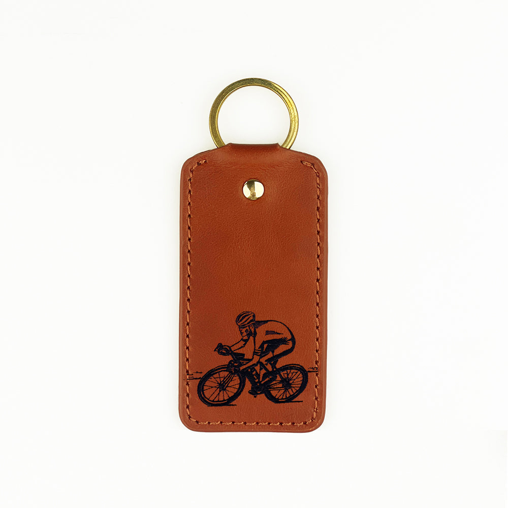 Brown leather keyring with black engraved cyclist design and gold-toned metal ring from selbrae house