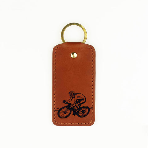Brown leather keyring with black engraved cyclist design and gold-toned metal ring from selbrae house