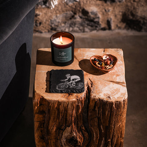 Black glass candle with lit flame on a single slate coaster featuring a green sillan label for stylish use