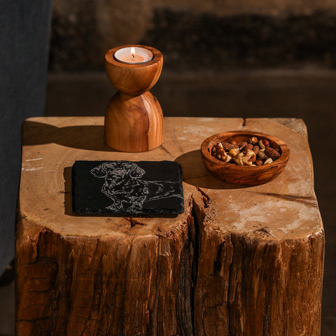 A rustic olive wood candle holder with polished finish and natural grain patterns next to a dachshund single slate coaster