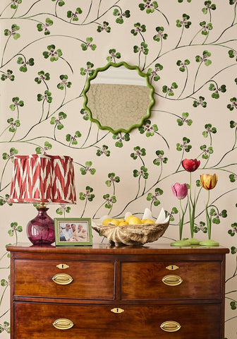 A green scalloped mirror with a decorative frame hangs above a wooden dresser near a dahlia pink tulip candleholder tole