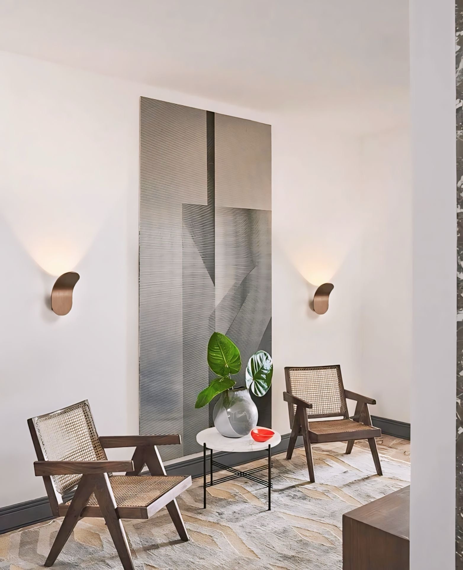 A sleek metallic silver vase with vertical ridges holding green leaves complements daisuke light wall lights design