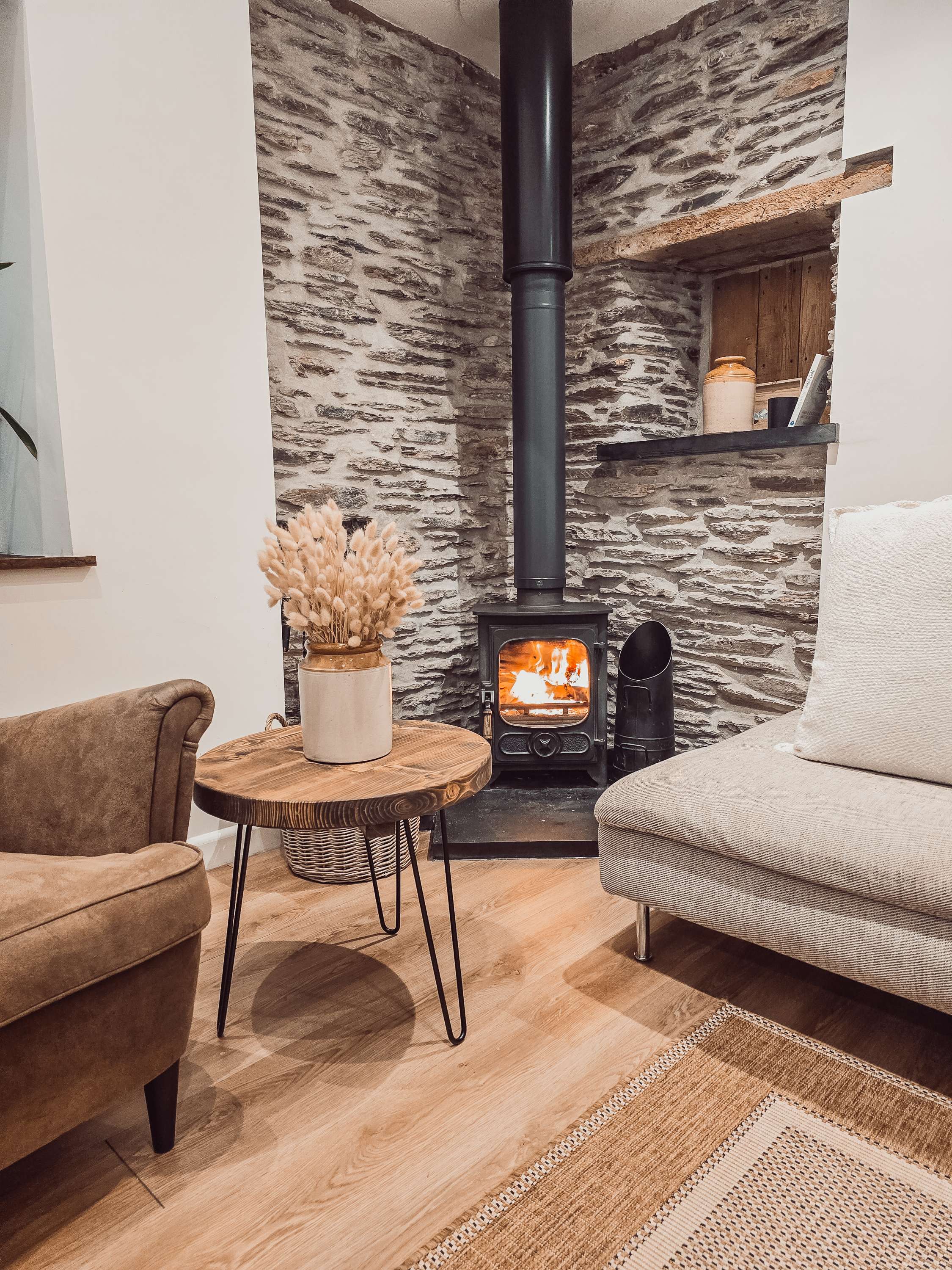 Black metal wood-burning stove with glowing flames beside dalva walnut round coffee table for cozy round coffee space
