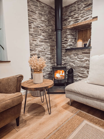Black metal wood-burning stove with glowing flames beside dalva walnut round coffee table for cozy round coffee space