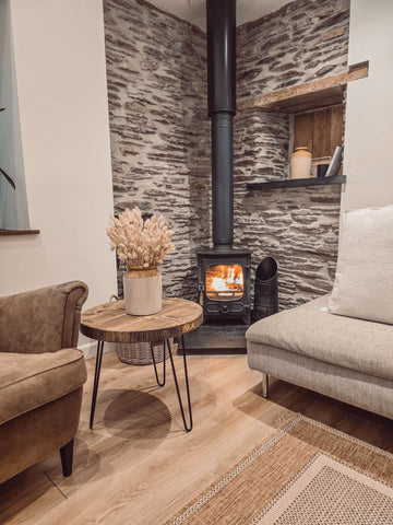 Black metal wood burning stove with glowing flames inside next to dalva walnut round coffee table and round coffee setup