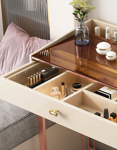 Beige damion dressing table with rose gold legs and mirrored top featuring an open drawer organized with cosmetics