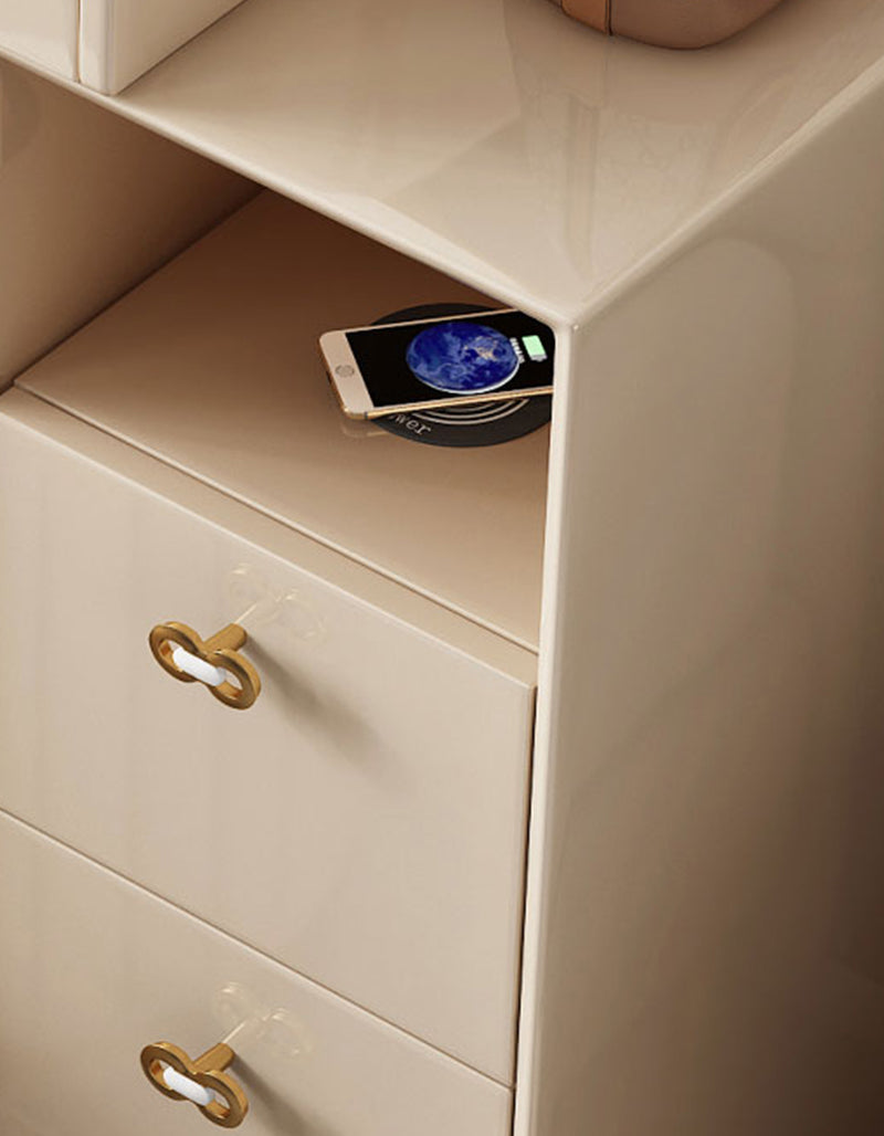 A sleek cream-colored damion dressing table nightstand with gold key-shaped pulls and wireless charging holding a smartphone