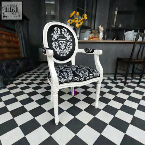 A white ornate bowler arm chair by dan gold with black skull and barrettes upholstered back and seat